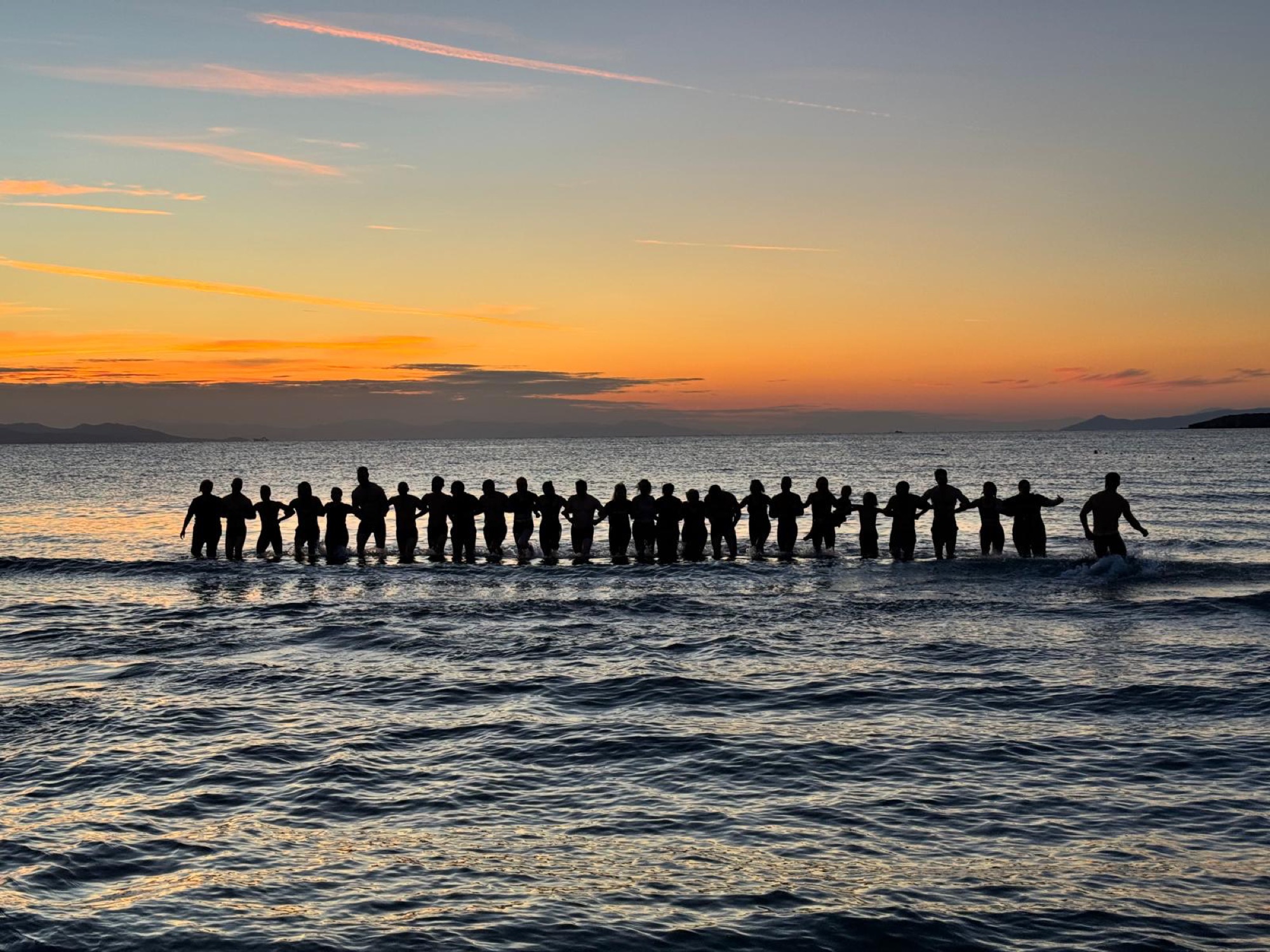 Workshop instructors linking arms in the sea at sunset, Athens