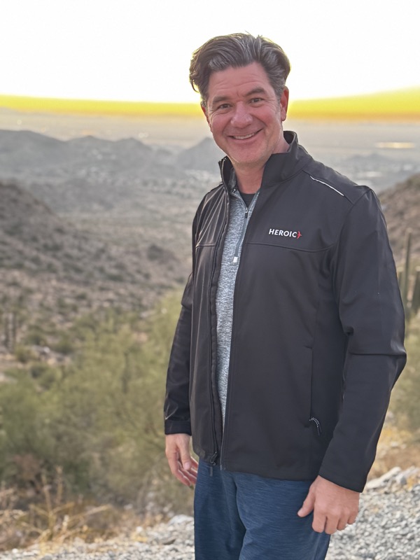 Bradley Lewis on a mountain summit at sunrise, in his Heroic jacket